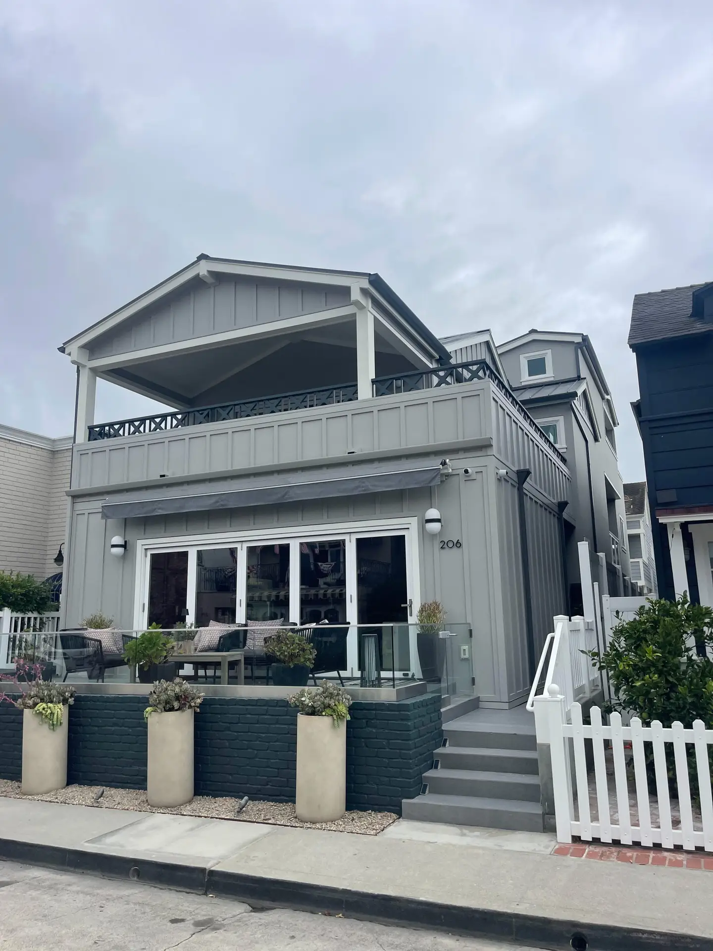 Gray two-story house with a large open upper balcony, white trim, and a glass-railed front patio; house number 206.
