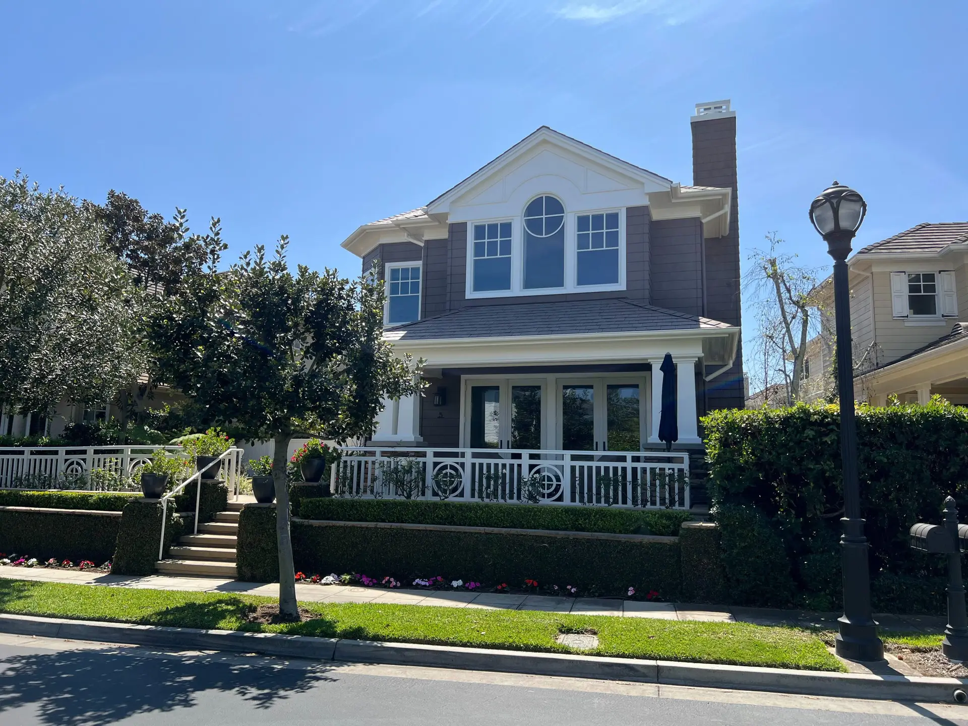 Two-story gray house with white trim, circular attic window, and a white railing porch with a manicured front yard.