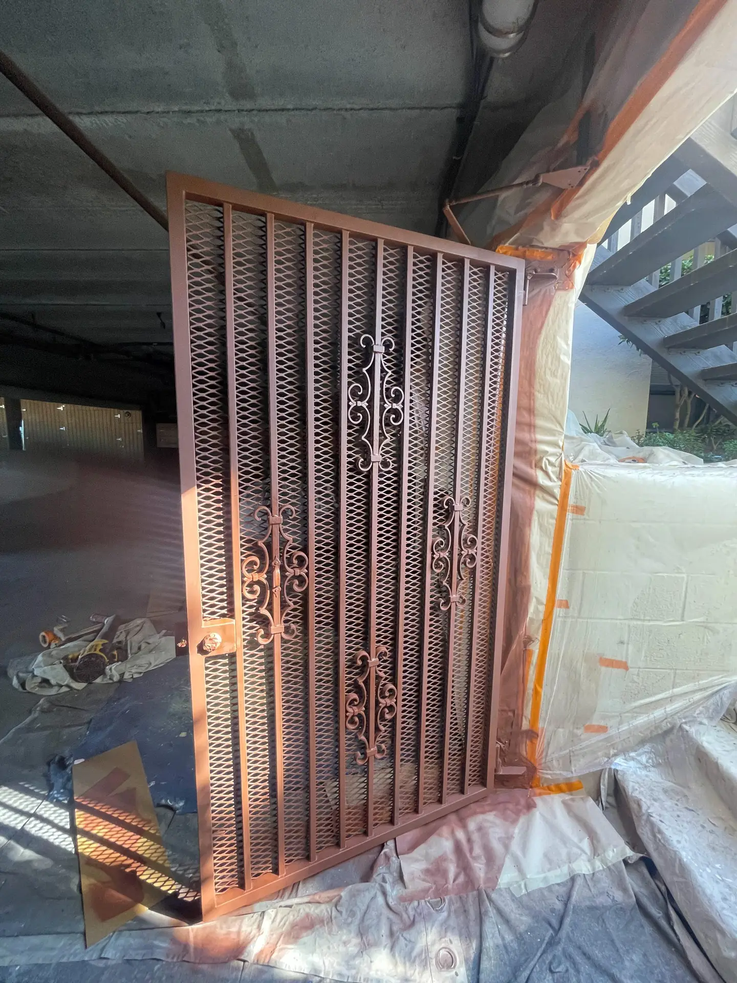 Decorative metal security gate with ornamental scrollwork leaning against a wall in a covered construction area covered in plastic sheets.