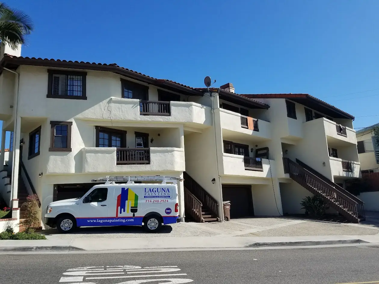 Two-story beige apartment building with dark trim and balconies; a painting company van parked in front.