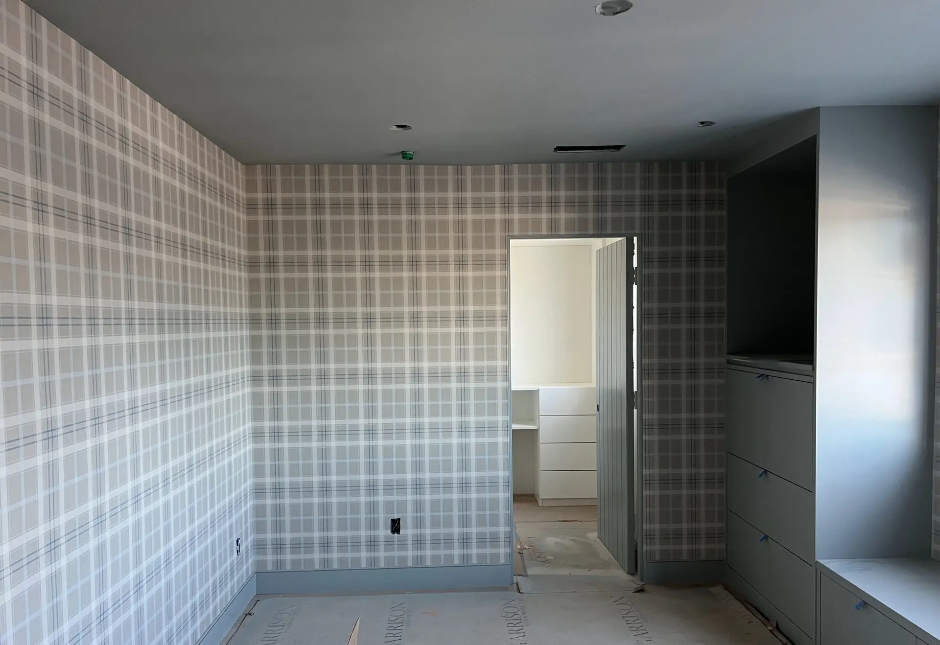 Room under renovation with plaid wallpaper, white built-in cabinets, and exposed ceiling cutouts.