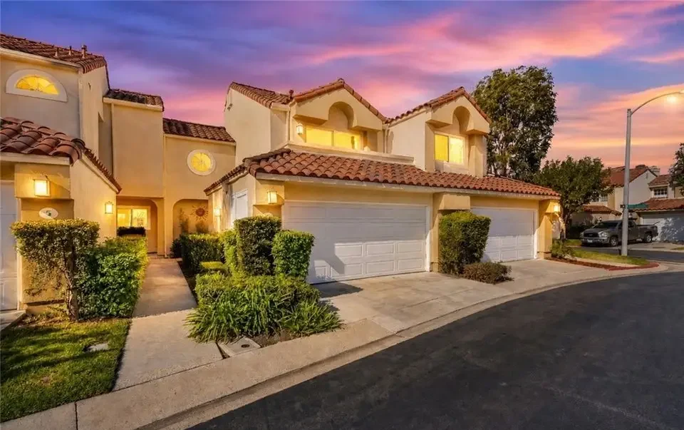 Row of beige stucco townhomes with red-tile roofs and attached garages at sunset