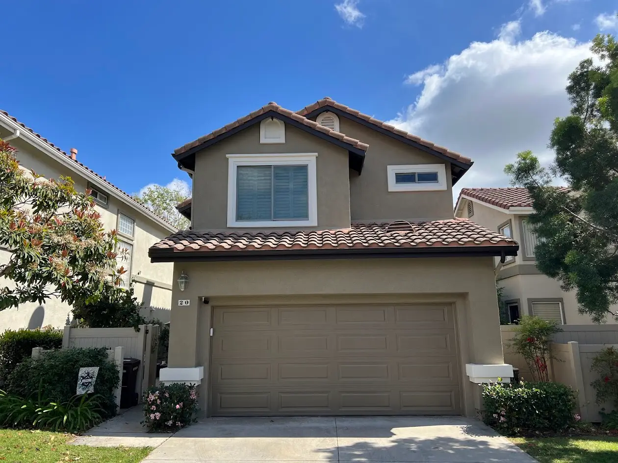 Front view of a two-story beige house with a tan tiled roof and a large double garage, under a bright blue sky.