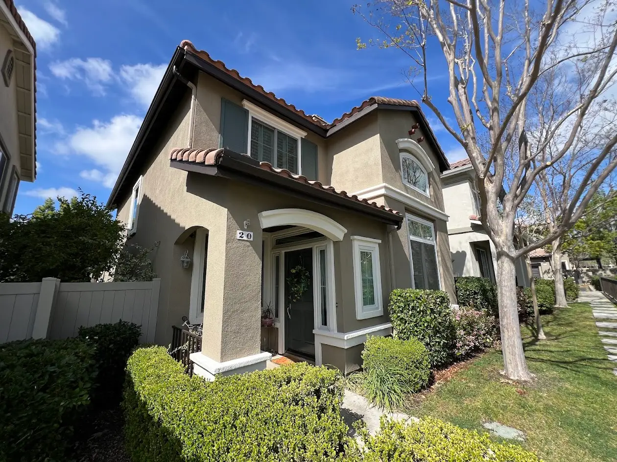 Front view of a beige two-story townhouse with a curved arch over the front door, trimmed hedges, and a clear blue sky.