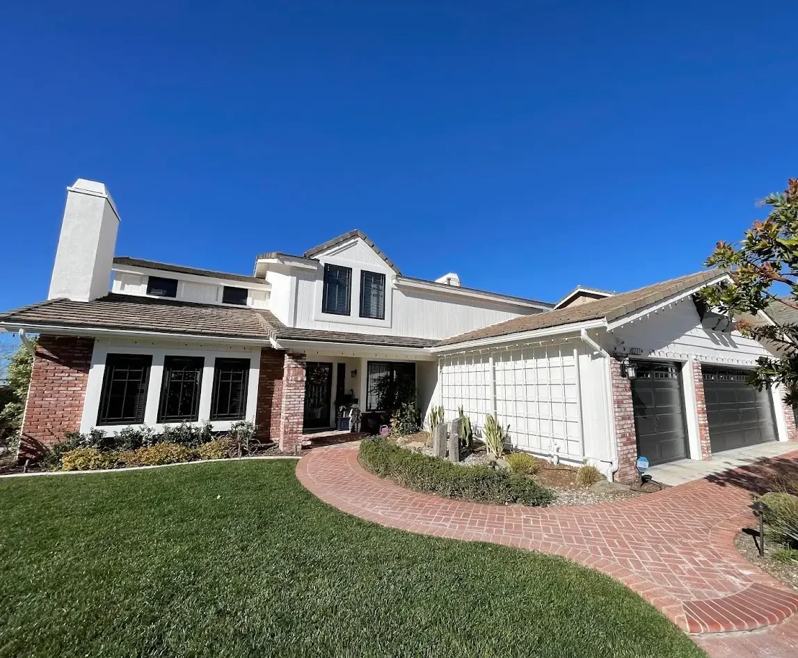Front view of a white and brick suburban house with a curved brick walkway and a three-car garage under a blue sky.