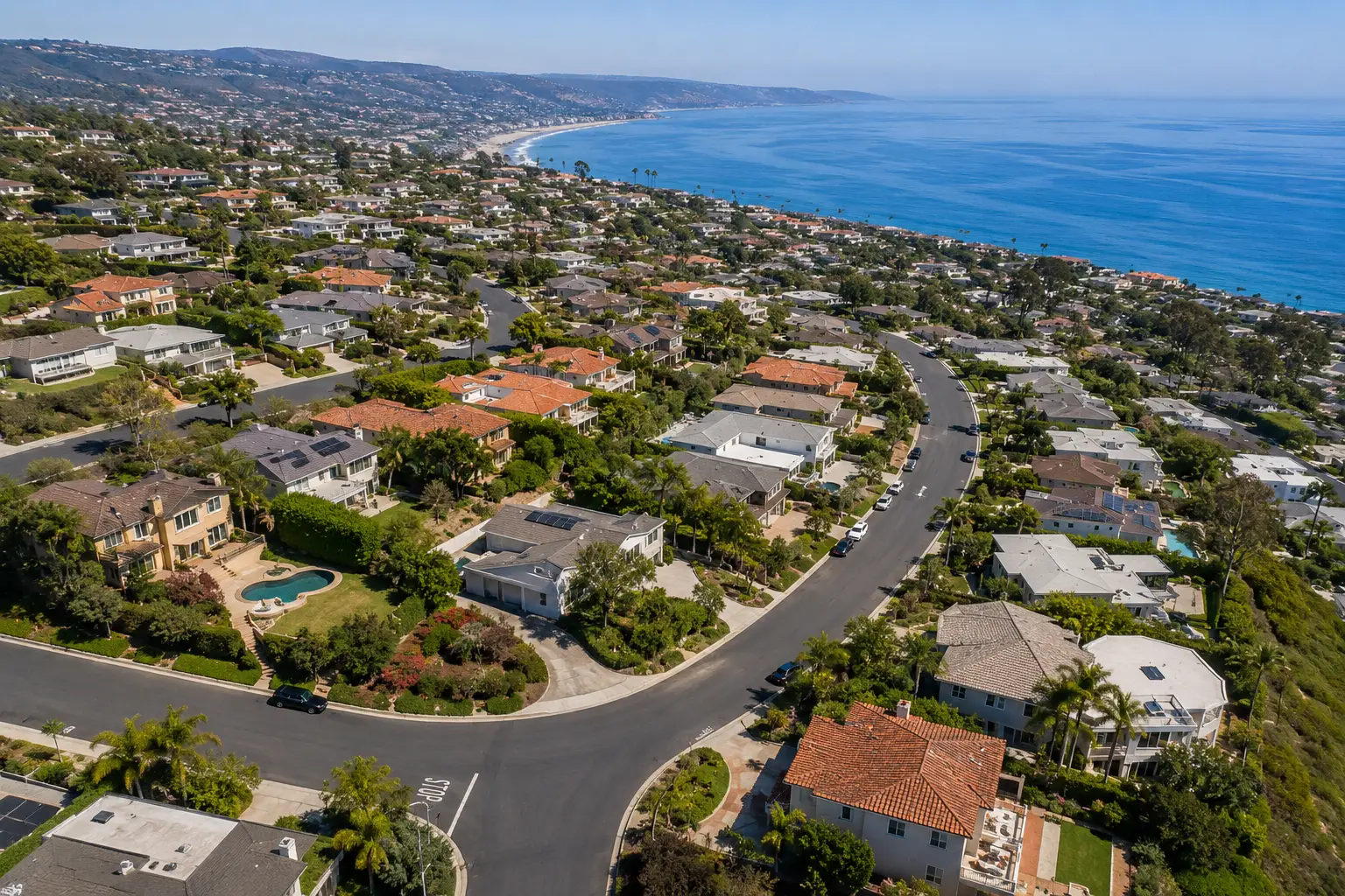 Coastal suburban neighborhood with winding streets and many houses, ocean shoreline in the distance.